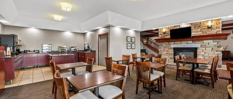 A spacious dining area with wooden tables and chairs, a kitchen with modern appliances, and a stone fireplace with a TV mounted above it.