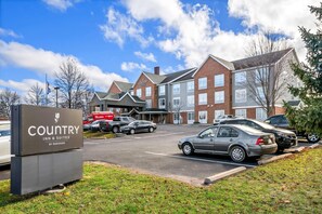 A Country Inn & Suites by Radisson with a parking lot, brick buildings, and a clear sky.