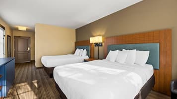 A hotel room with two beds, a desk, a lamp, and a door.