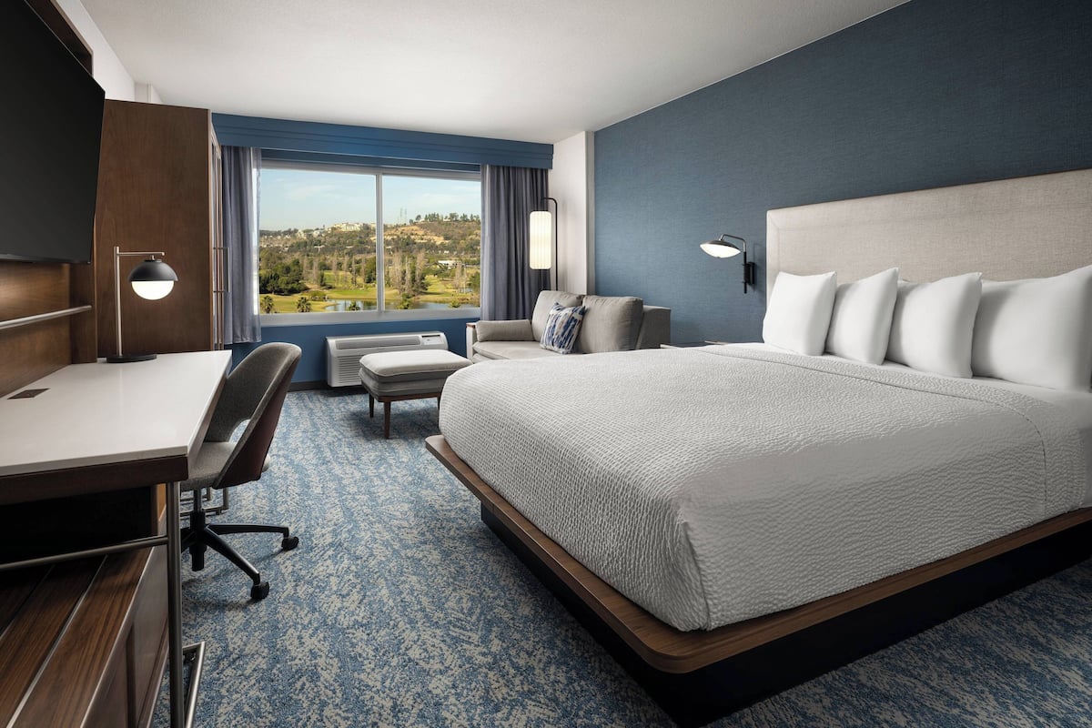 Une chambre d’hôtel avec un grand lit, un bureau, une chaise et une vue sur un paysage.