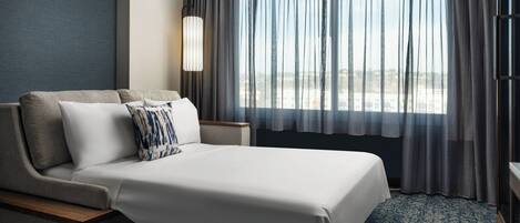 A hotel room with a bed, a sofa, a nightstand, and a window with curtains.