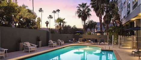 A pool area with lounge chairs, palm trees, and a building in the background.