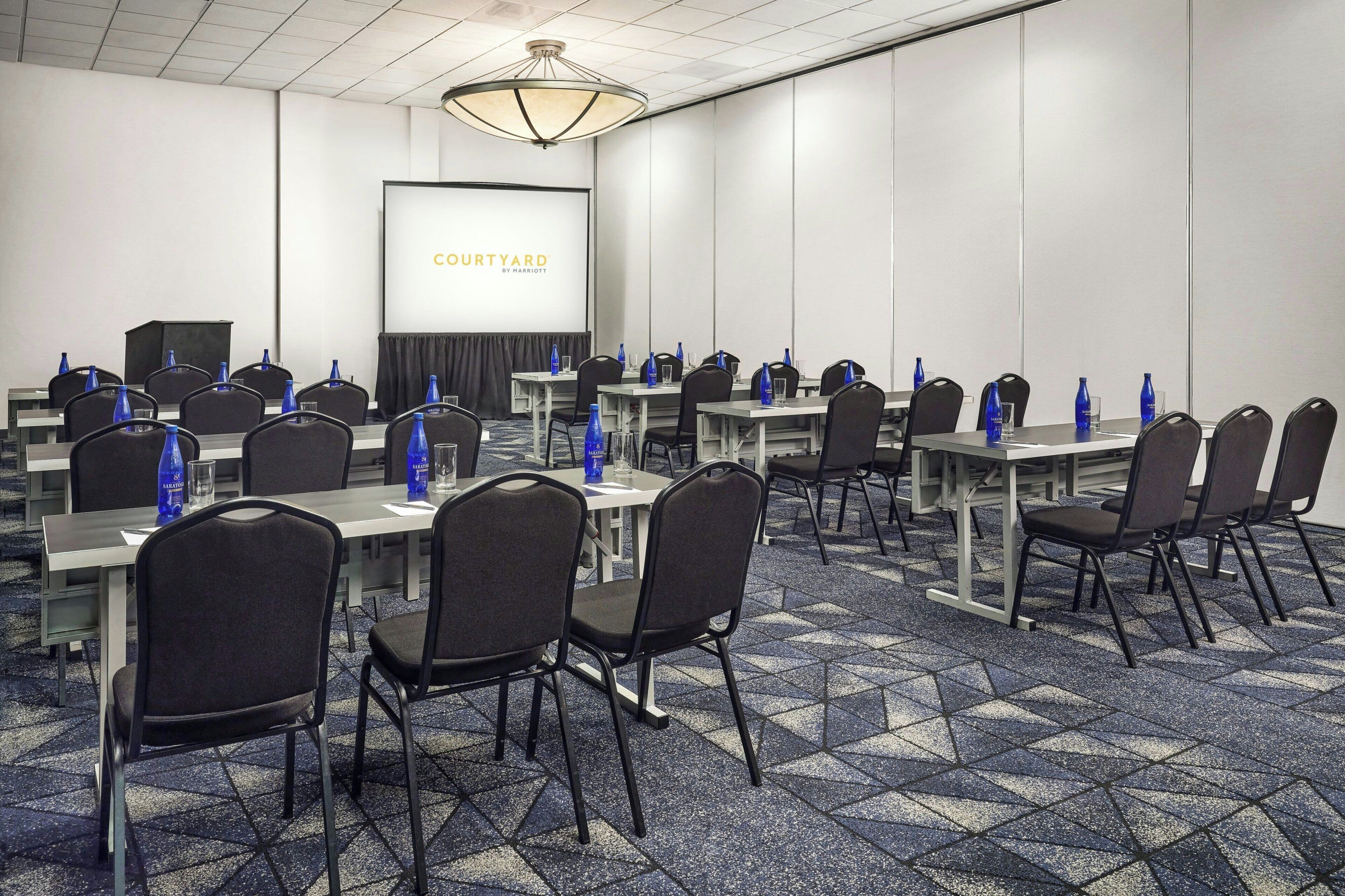 A conference room with multiple tables and chairs, a projector screen, and a carpeted floor.