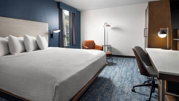 Una habitación de hotel con una cama, un sillón naranja, un escritorio y una lámpara de pie.