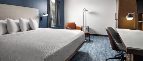 A hotel room with a bed, an orange chair, a desk, and a floor lamp.