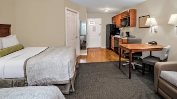 Habitación de hotel con cama, escritorio, silla, microondas, refrigerador y puerta que da a un baño.