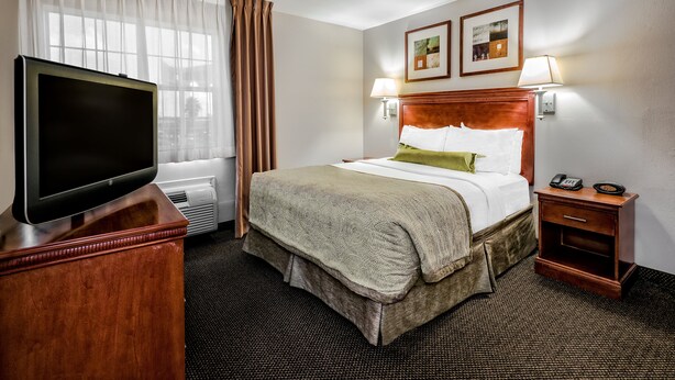 Hotelkamer met een bed, bedlampen, een televisie op een houten standaard en een klein nachtkastje met een telefoon.