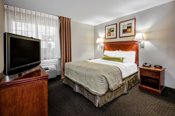 Una habitación de hotel con una cama, lámparas de noche, un televisor sobre un mueble de madera y una mesita de noche con un teléfono.