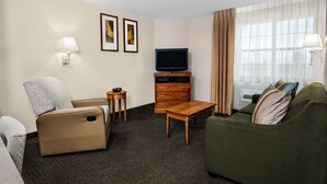 Een hotelkamer met een bank, fauteuil, televisie, houten kast en een klein tafeltje.