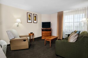Habitación de hotel con sofá, sillón, televisión, mueble de madera y una mesita.
