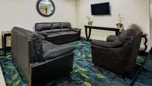 A living room with a sofa, armchairs, a flat-screen TV, a mirror, and a small table with plants.