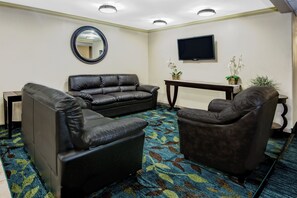 Una sala de estar con un sofá, sillones, un televisor de pantalla plana, un espejo y una pequeña mesa con plantas.