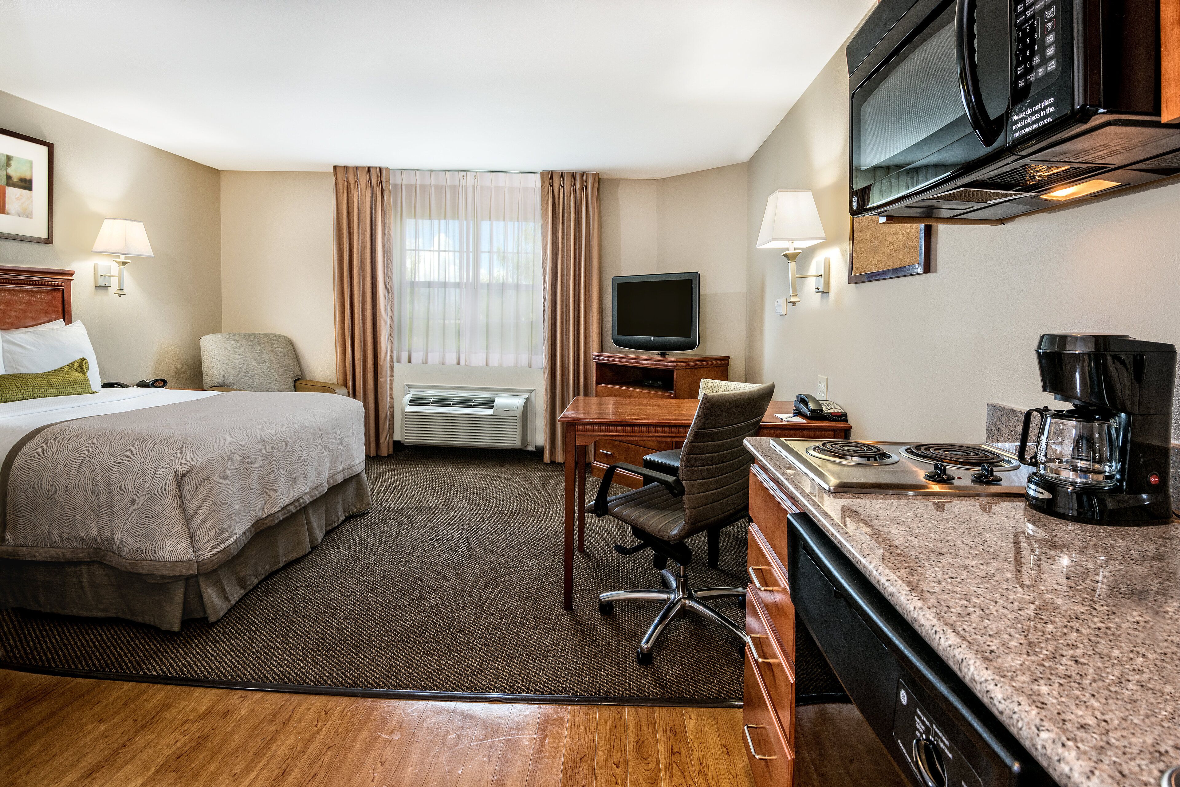 A hotel room with a bed, desk, chair, television, microwave, and coffee maker.