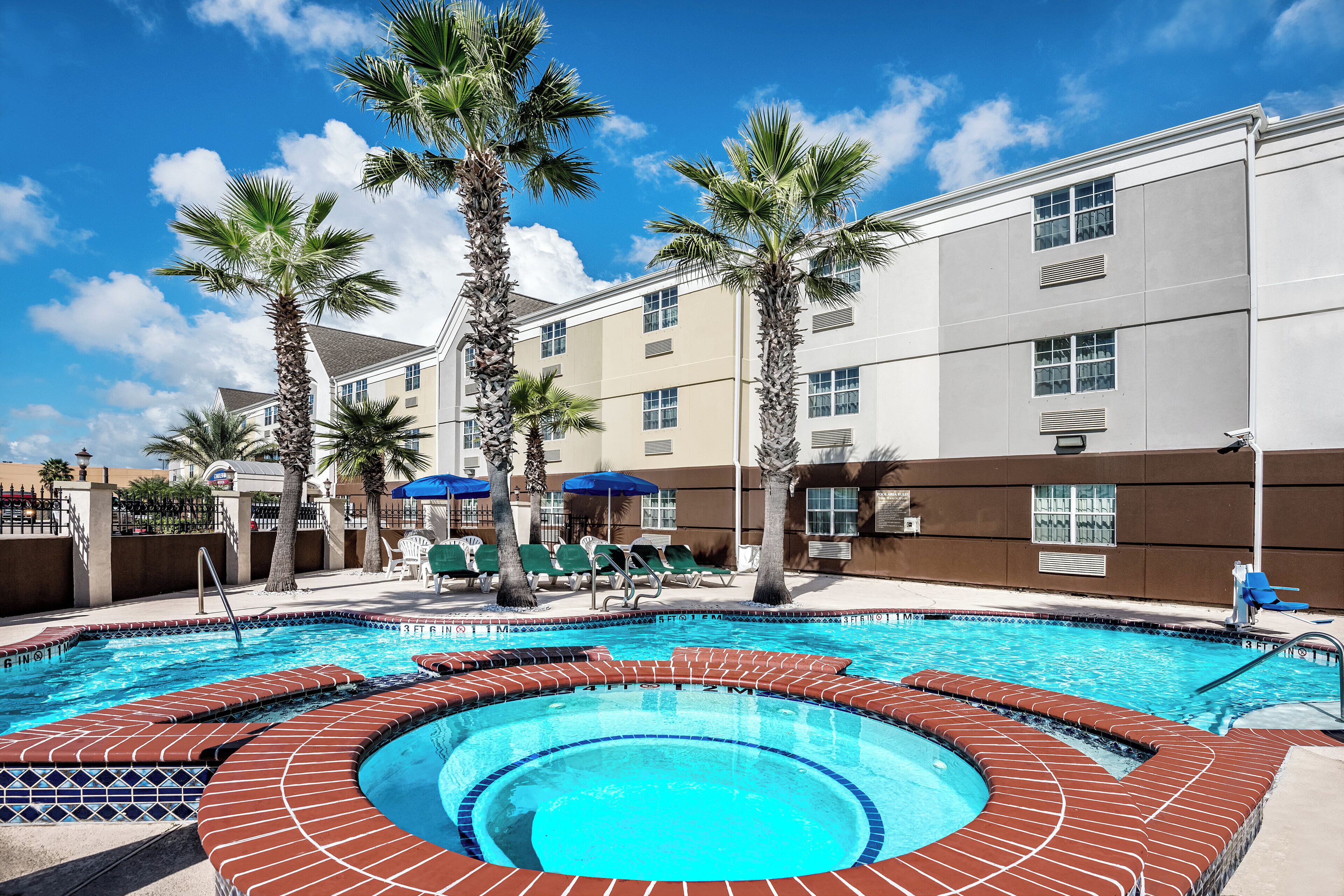 A hotel pool area with a hot tub, palm trees, and lounge chairs.