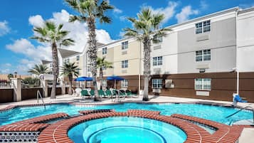 A hotel pool area with a hot tub, palm trees, and lounge chairs.