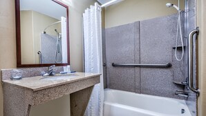 Een badkamer met een bad, douche, wastafel en spiegel.