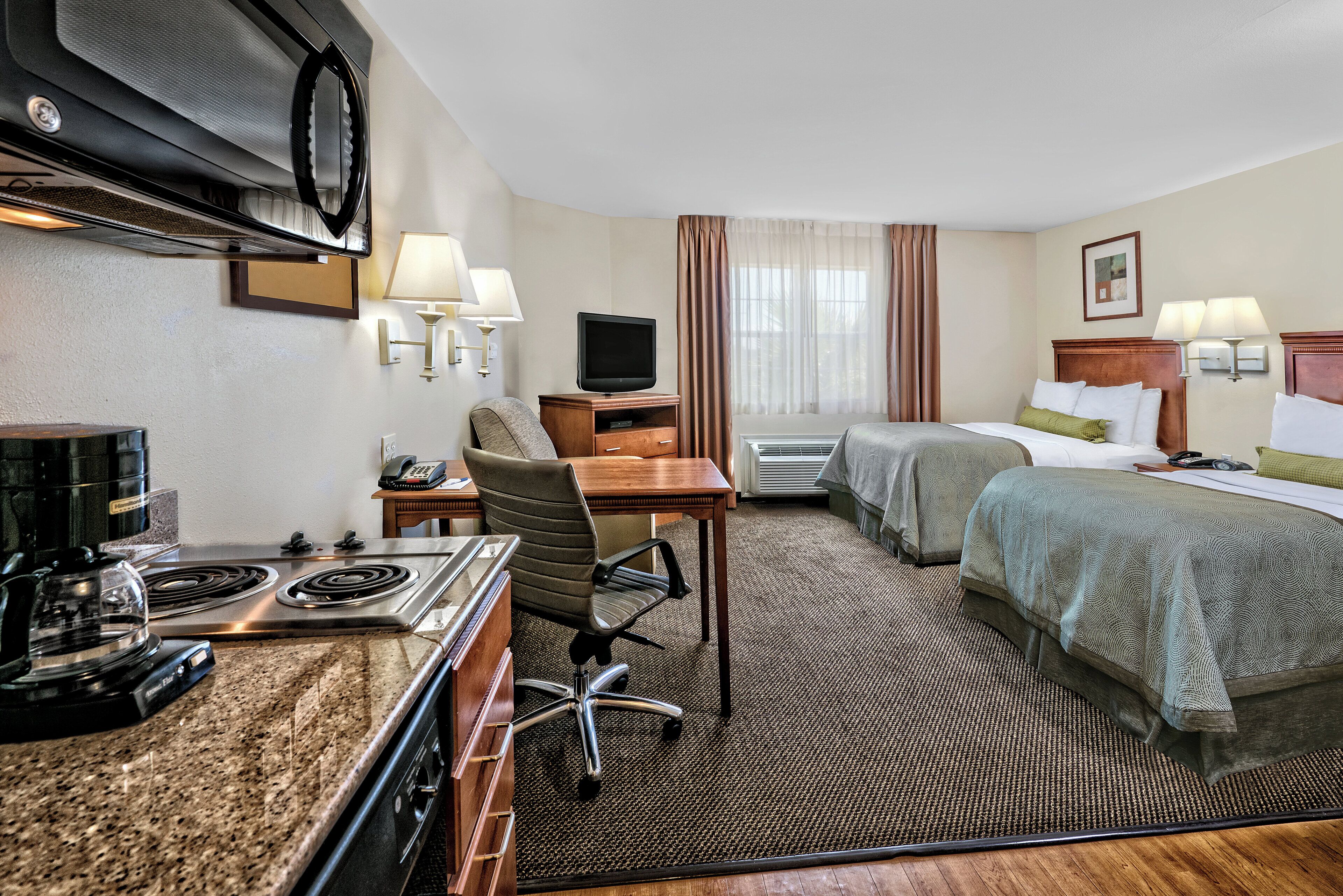 Een hotelkamer met een kitchenette, een bed, een bureau en een televisie.