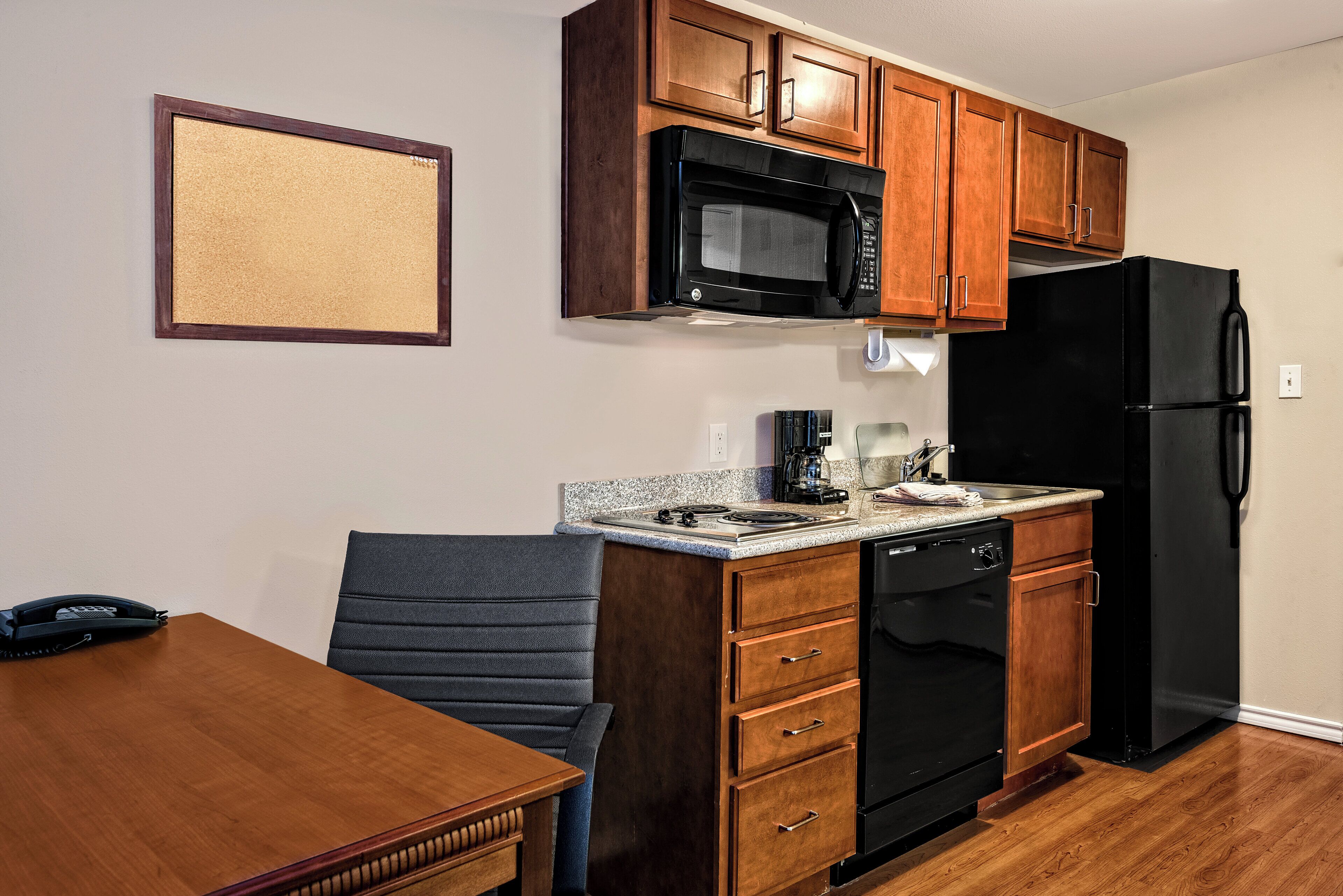 A compact kitchen with wooden cabinets, a black microwave, a black refrigerator, and a built-in dishwasher.