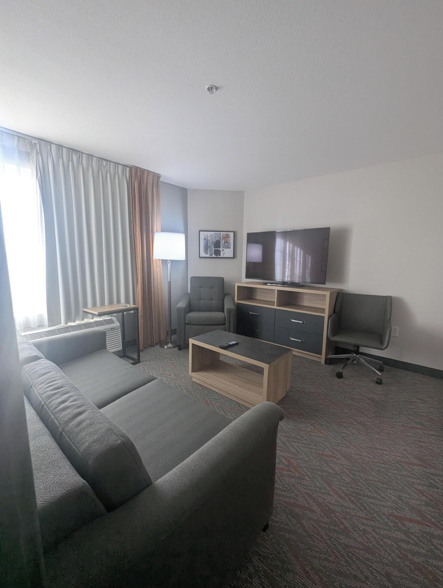 A hotel room with a sofa, a TV, a desk, and a chair.