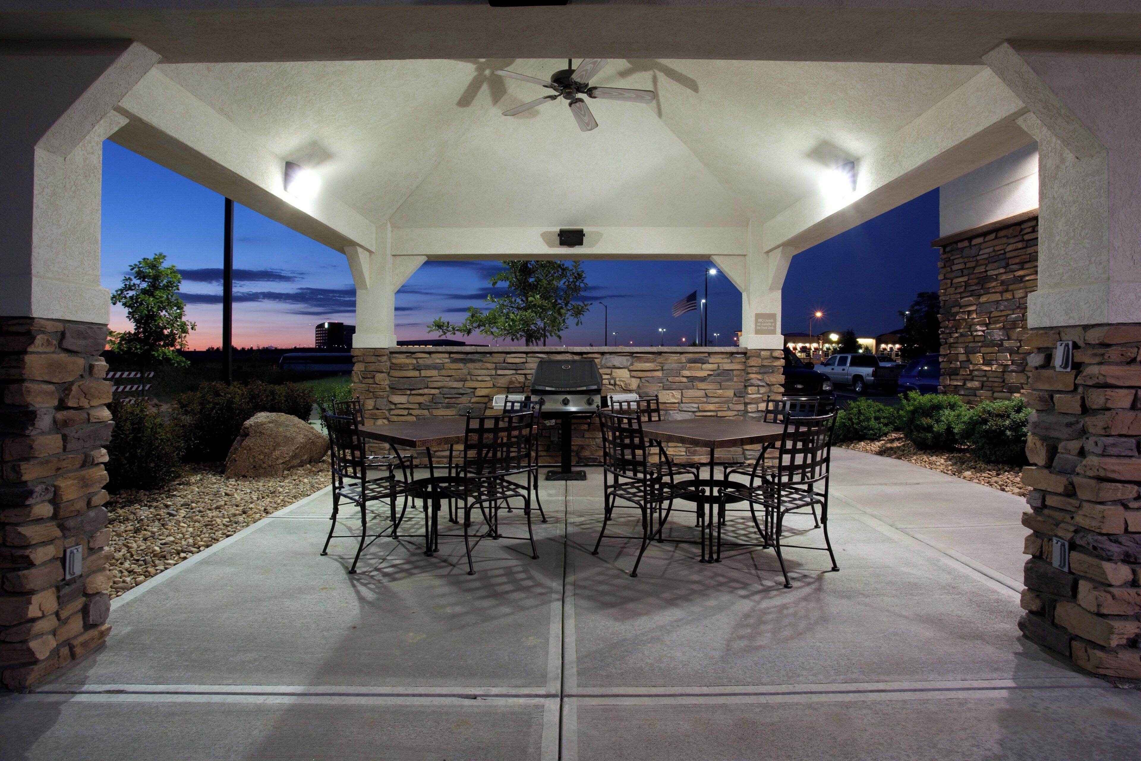 An outdoor patio with a stone wall, a table with chairs, and a ceiling fan.