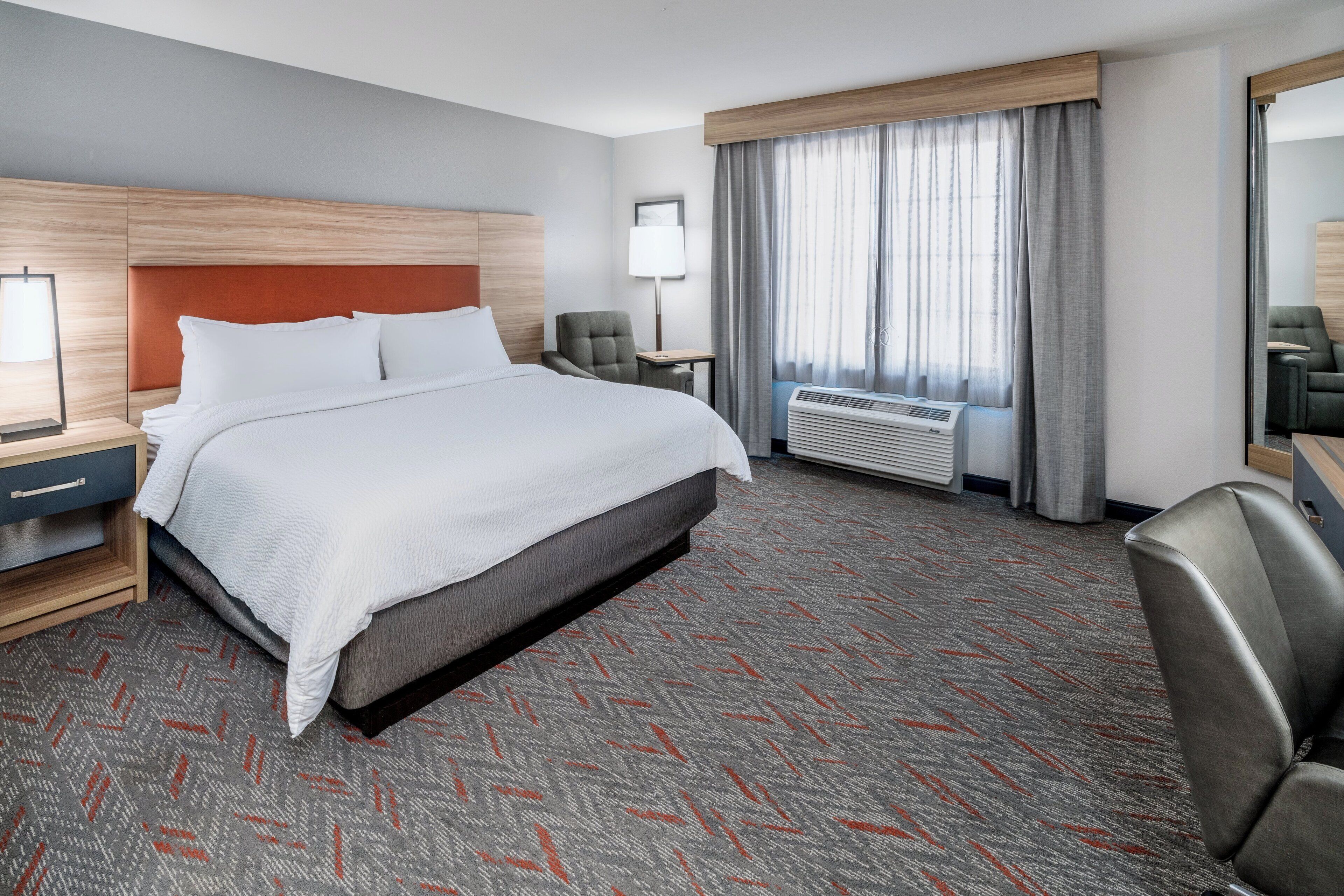 A hotel room with a large bed, a desk, a chair, a lamp, and a window with curtains.