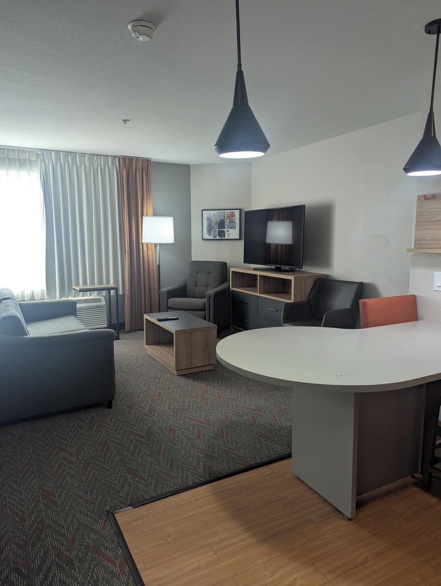 Una habitación de hotel moderna con sofá, una mesita de centro, televisión y una mesa redonda para comer.