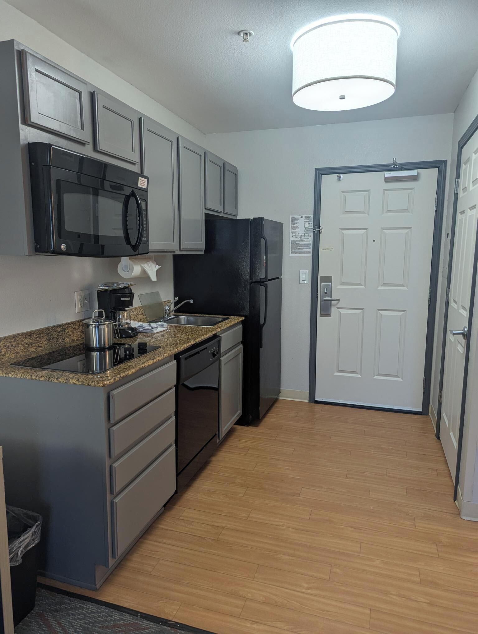 A compact kitchen with a microwave, refrigerator, sink, and granite countertop.