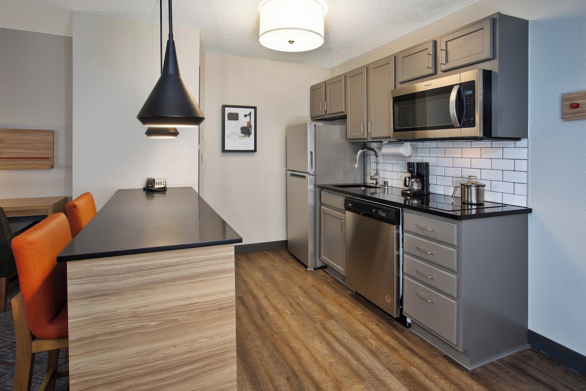 Una cocina moderna con una isla central, electrodomésticos de acero inoxidable y una lámpara colgante.