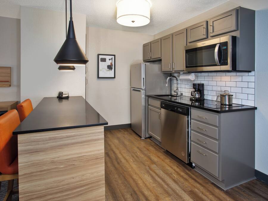 A modern kitchen with a central island, stainless steel appliances, and a black pendant light.