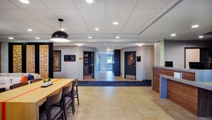 A hotel lobby with a reception desk, a seating area with a long table and chairs, and a corridor leading to other rooms. - Candlewood Suites Kenosha – Pleasant Prairie by IHG (Kenosha)