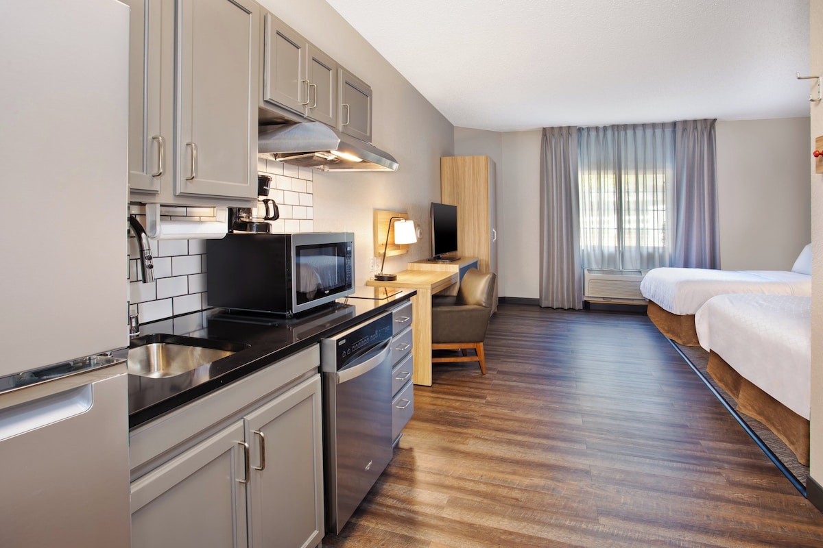 Una habitación de hotel compacta con kitchenette, una cama, un escritorio y un televisor.