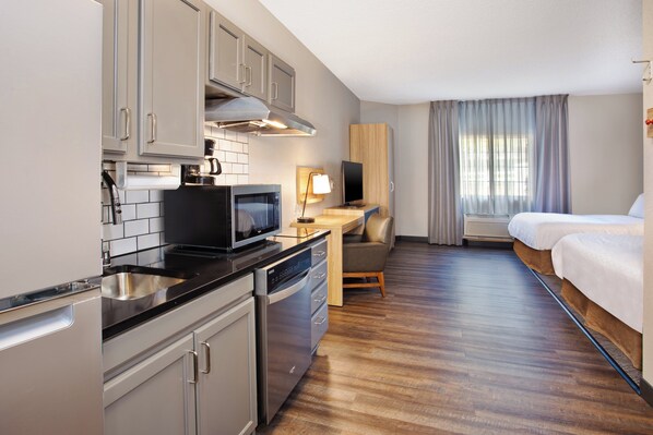 Una habitación de hotel compacta con kitchenette, una cama, un escritorio y un televisor.