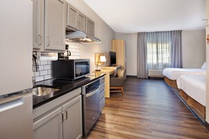 Una habitación de hotel compacta con kitchenette, una cama, un escritorio y un televisor.