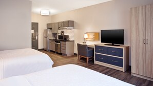 A hotel room with two beds, a kitchenette, a desk with a chair, a television, and a wardrobe.