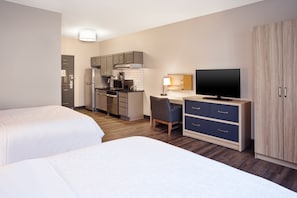Habitación de hotel con dos camas, kitchenette, escritorio con silla, televisor y armario.