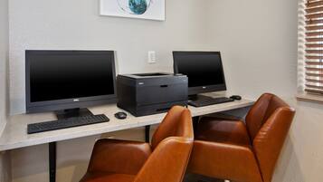 Un espacio de trabajo con dos monitores Dell, una impresora, un teclado y dos sillones de cuero.