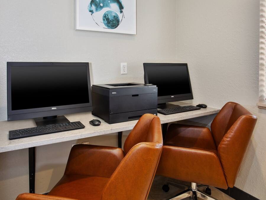 Un espacio de trabajo con dos monitores Dell, una impresora, un teclado y dos sillones de cuero.