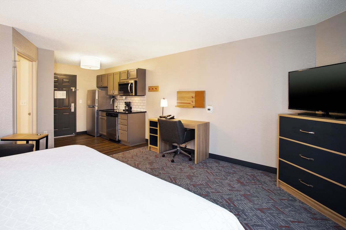 Una habitación de hotel con cama, escritorio, televisión, armario y kitchenette.