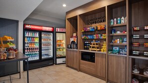 A snack bar with a Coca-Cola refrigerator, a Candlewood Cupboard, and shelves stocked with snacks and condiments. - Candlewood Suites Kenosha – Pleasant Prairie by IHG (Kenosha)