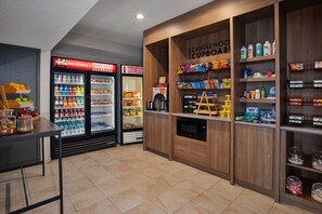 Una barra de aperitivos con un refrigerador de Coca-Cola, un Candlewood Cupboard y estantes llenos de bocadillos y condimentos.