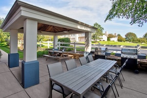 Un patio exterior con zona de estar cubierta, una parrilla y una mesa con sillas.