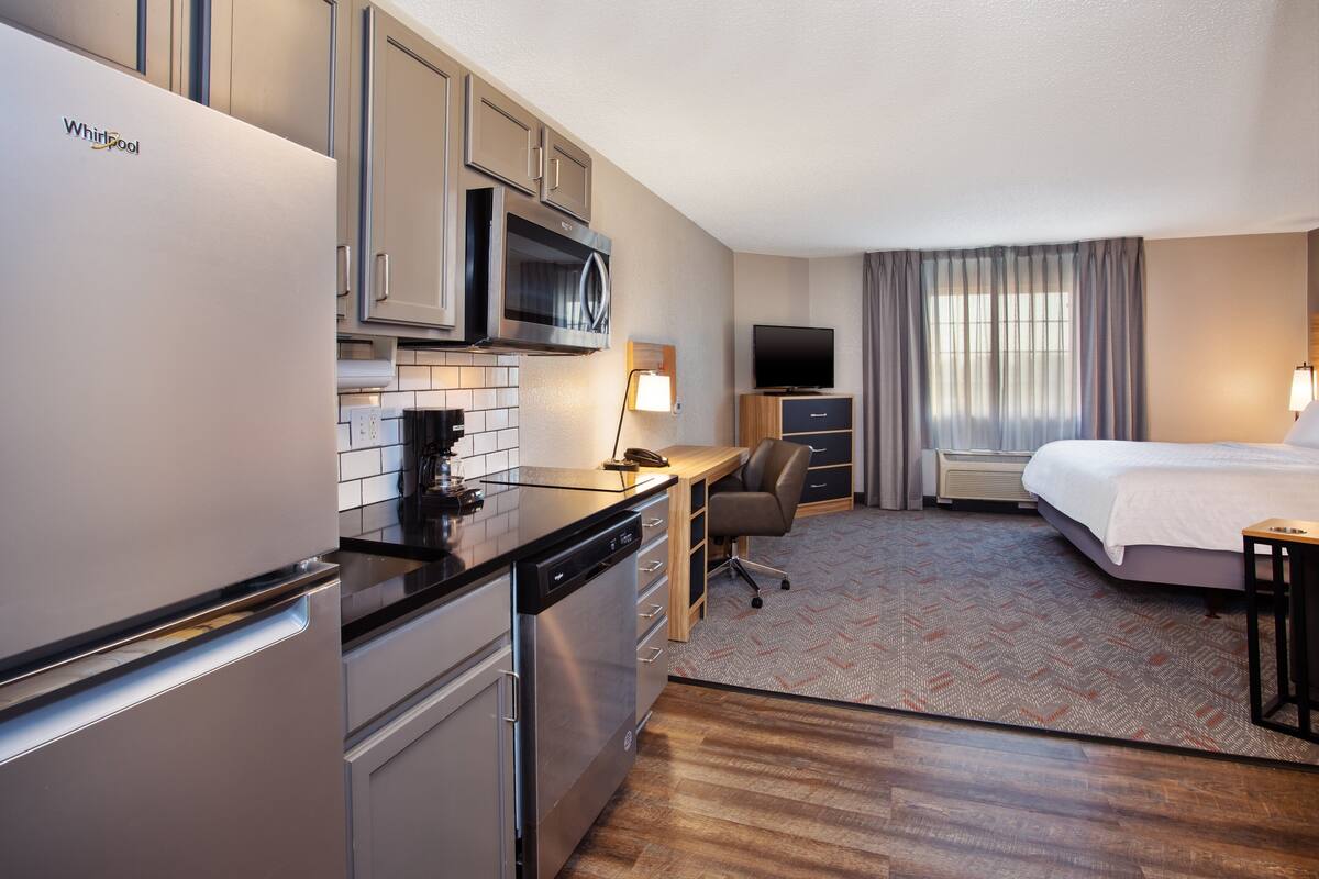 Ein kompaktes Hotelzimmer mit Küchenzeile, einem Bett, einem Schreibtisch mit Stuhl und einem Fernseher.