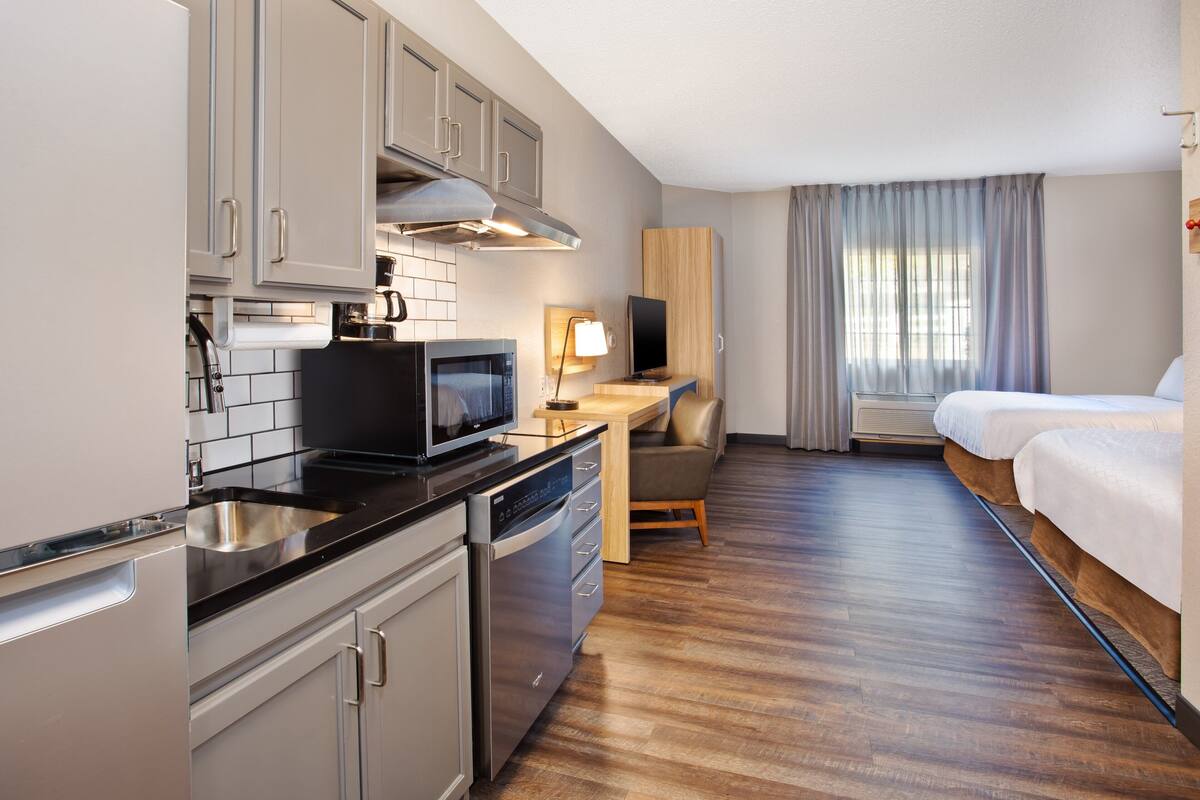 Ein kompaktes Hotelzimmer mit Küchenzeile, einem Bett, einem Schreibtisch und einem Fernseher.