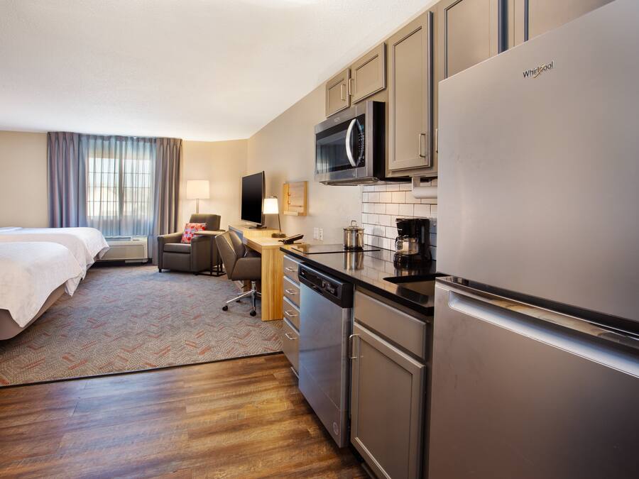 Habitación de hotel con cama, escritorio, microondas, refrigerador y lavavajillas.