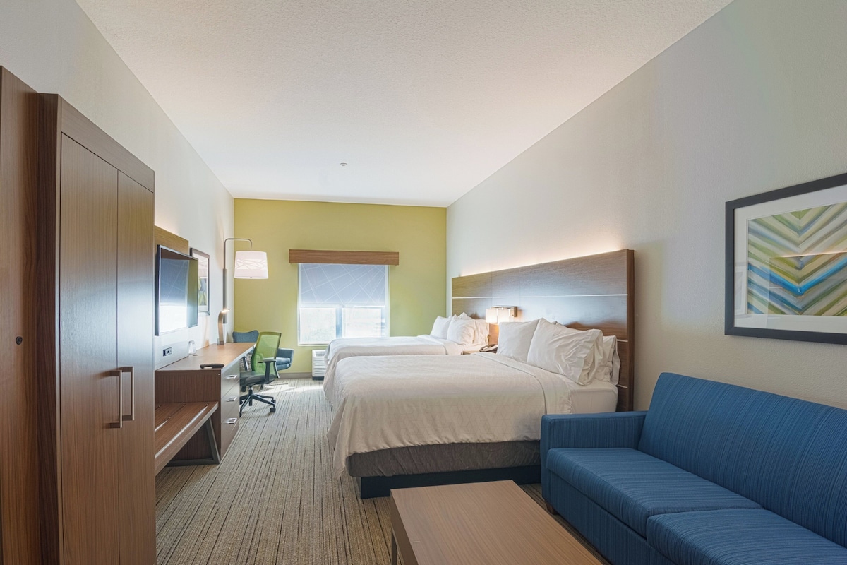 A hotel room with two beds, a desk, a chair, a sofa, and a TV.