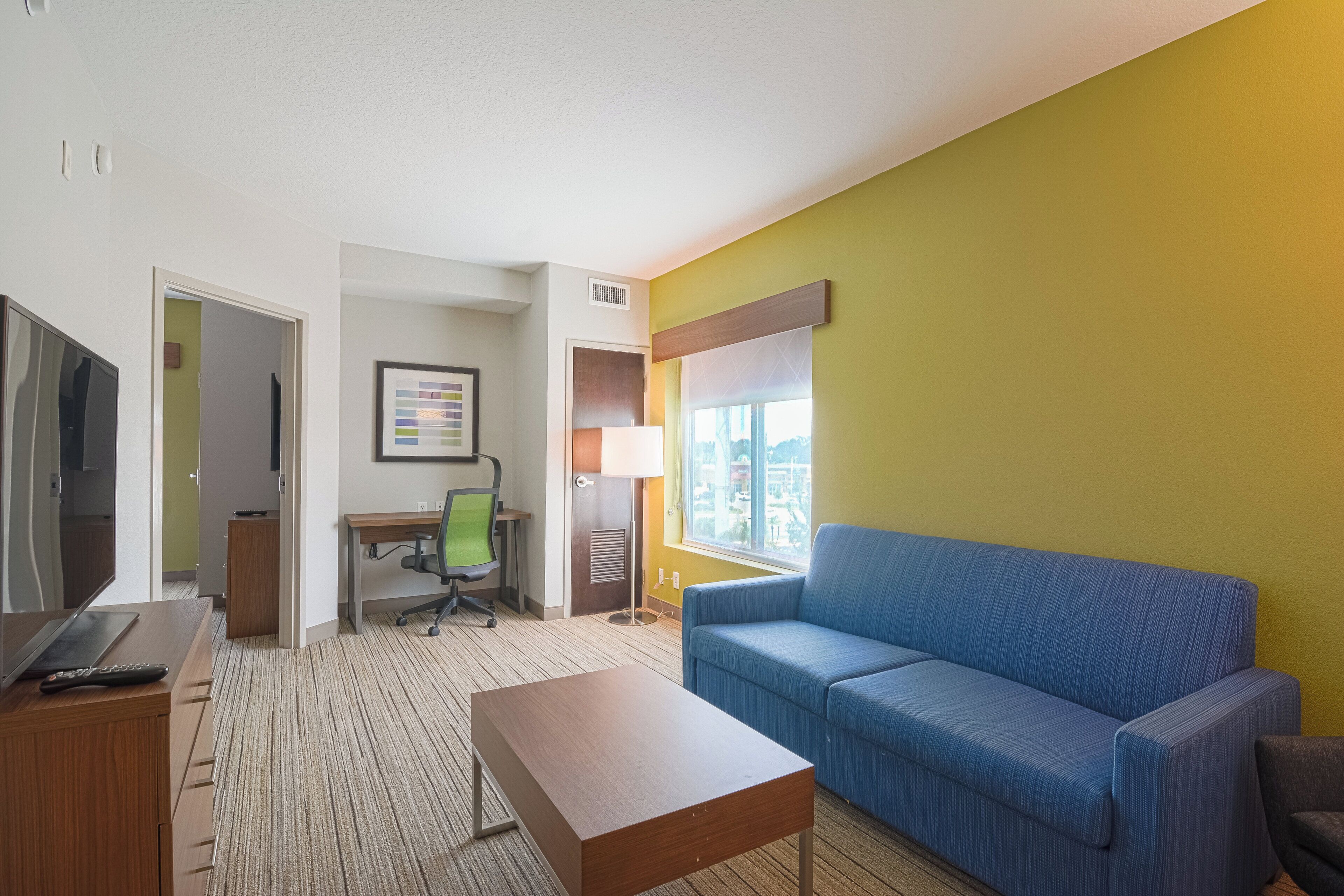A hotel room with a bed, a desk, a chair, a television, and a window.