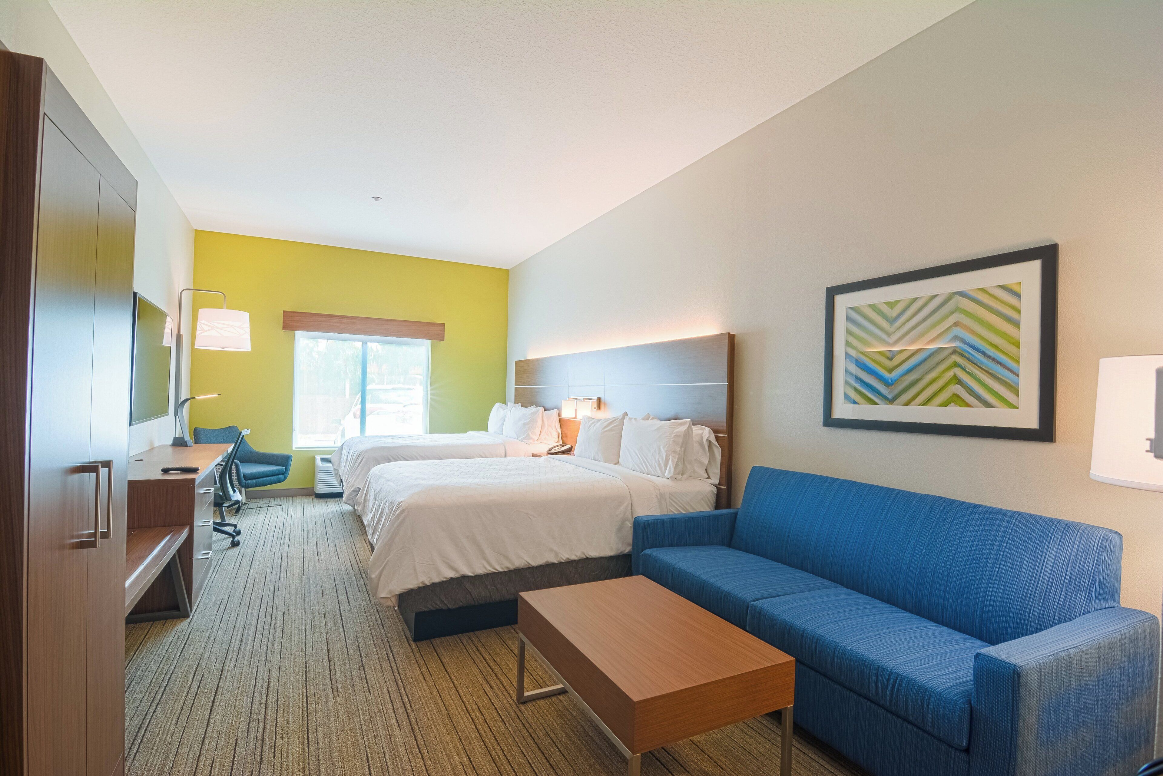 Ein Hotelzimmer mit zwei Betten, einem Schreibtisch, einem blauen Sofa und einem Gemälde an der Wand.
