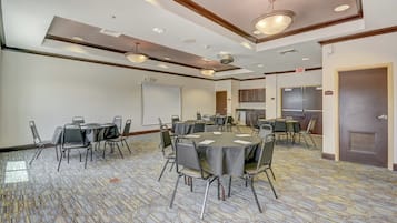 A conference room with multiple tables and chairs, a projector screen, and a kitchen area.