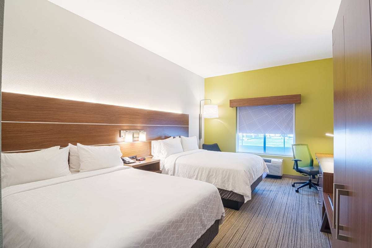 Ein Hotelzimmer mit zwei Betten, einem Schreibtisch, einem Stuhl, einem Nachttisch und einem Fenster mit Blick.