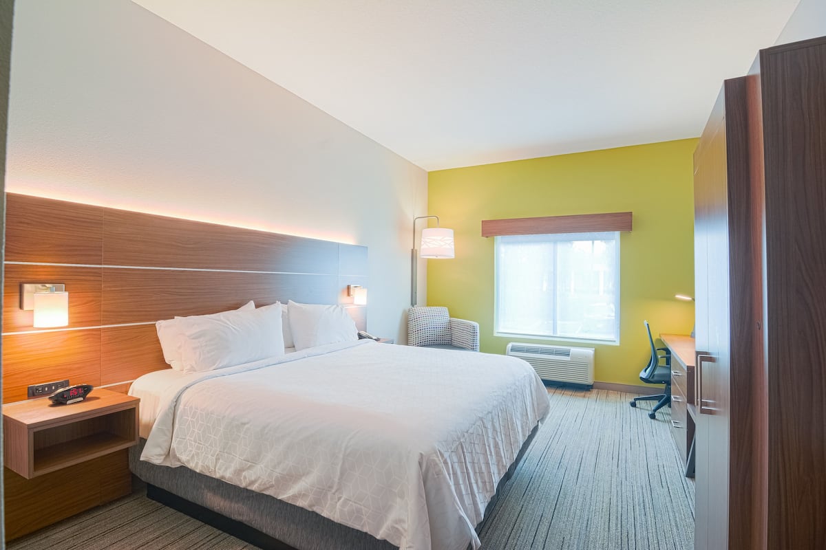 Ein Hotelzimmer mit Bett, Nachttisch, Lampe, Stuhl, Schreibtisch und Fenster.